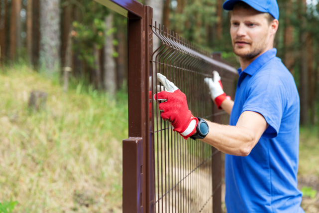 Worker installing welded metal mesh fence